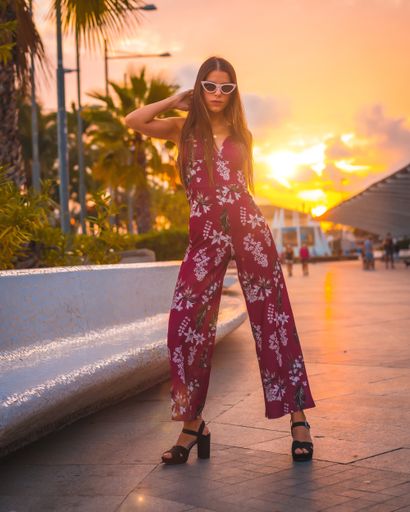 A beautiful brunette female in a maroon floral dress and white sunglasses posing during golden hour