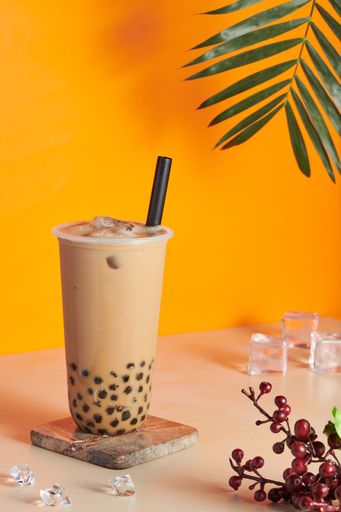 A plastic cup filled with fresh and tasty bubble milk tea on a wooden coaster on the table