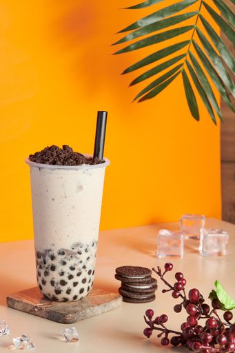 A plastic cup filled with fresh bubble milk tea with crushed cookie chocolate on the top