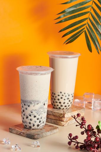 Two plastic cups filled with fresh and tasty bubble milk tea on a wooden coaster on the table