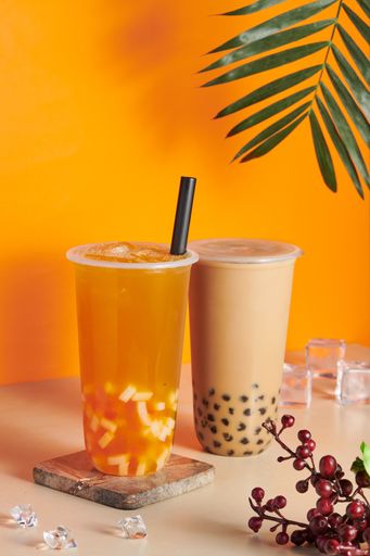Two plastic cups filled with fresh and tasty orange juice and bubble milk tea on the table