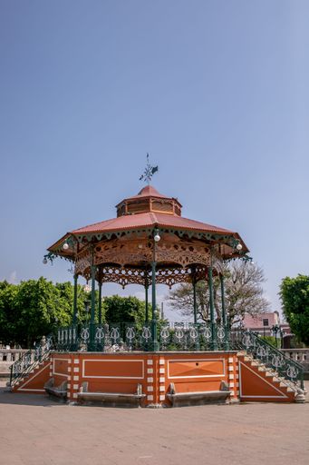 An outdoor gazebo situated in a lush, green park, surrounded by tall trees