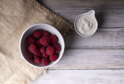 A bowl of raspberries served with natural white cream on a wooden table