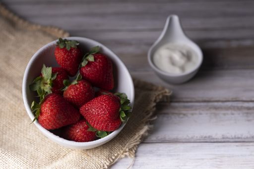 A bowl of fresh strawberries served with natural white cream on a wooden table