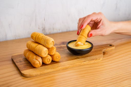 Venezuelan tequenos cheese fingers piled high on a wooden table and hand with tequeno dipping it in the sauce.