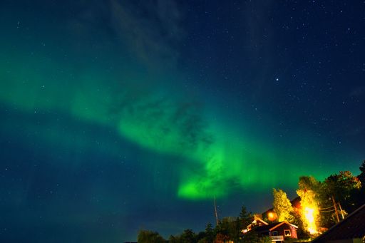 A majestic aurora borealis illuminates the sky above a rustic wooden cabin, emitting a beautiful green and yellow glow