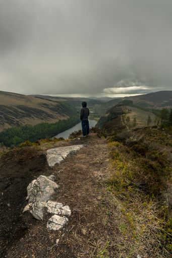 A male standing on top of a mountain with a lake in the background at Glendalough Wicklow
