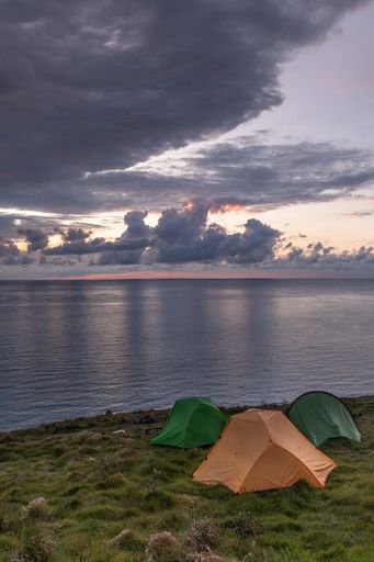 A vertical shot of three tents on cliffs at dawn in Greystones, Ireland