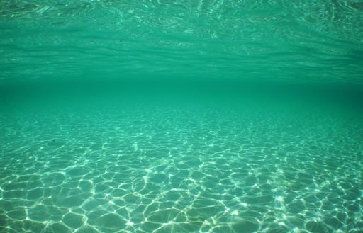 A plain background of a seabed with sunlight shining on the bottom through the waves