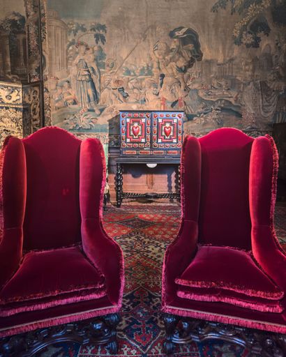 This image showcases a room filled with oriental art, featuring two ornately carved wooden chairs upholstered in a vibrant red fabric