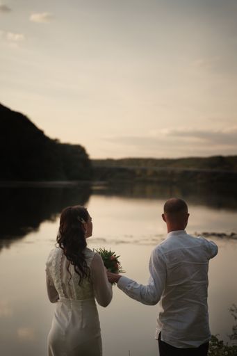 A vertical shot of a newly wedded couple standing by the lakeshore after an intimate wedding