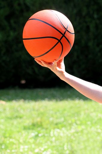 A vertical shot of a female holding a basketball ball in a field