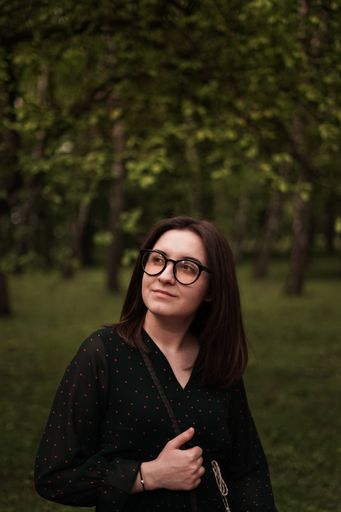 A shallow focus of a beautiful brunette female wearing glasses and posing in the park
