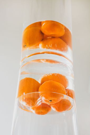 the mandarins dipped in water inside a transparent jar reflected in a mirror - white background