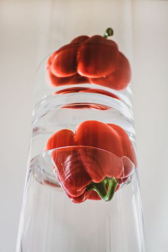 a bell pepper dipped in water inside a transparent jar reflected in mirror - white background
