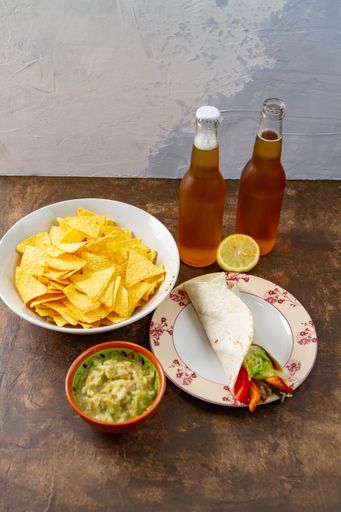 a vertical shot of two bottles of beer with chips, salad, sliced lemon and vegetable tortilla wrap