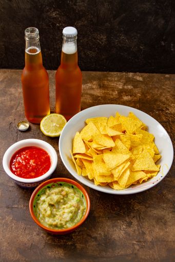 a vertical shot of two bottles of beer with chips, salad and ketchup on bowls with a sliced lemon