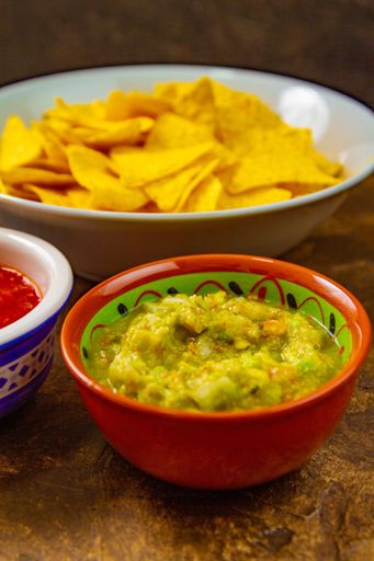 A vertical shot of chips, vegetable salad and ketchup in bowls on a brown table