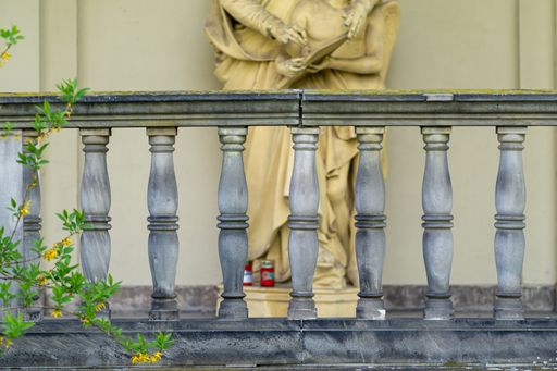 A stone railing in front of a statue of a wise old man and a child holding a book