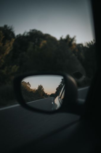 A vertical shot of a car side-view mirror with the road reflection in it
