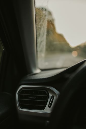 A vertical shot of a car heater with sunset visible behind windshield in the background