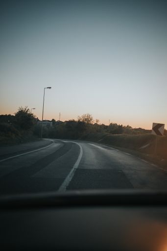 A vertical shot of a curving road seen through the windshield of a car during sunset