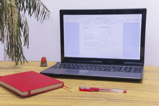A closeup shot of a red notebook and an open laptop on an office desk