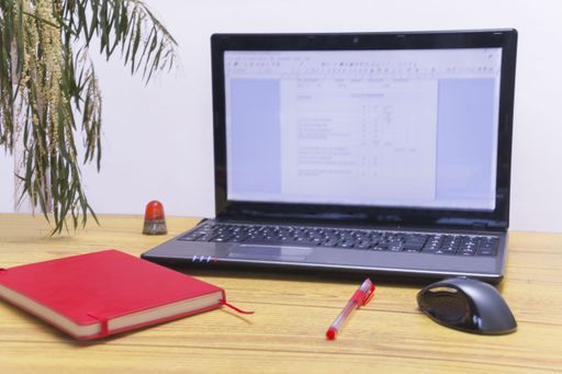 A closeup shot of a red notebook and an open laptop on an office desk