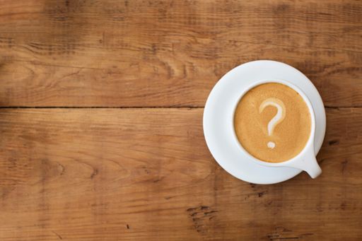A top view of a cup of coffee with a question mark in the foam on a wooden table