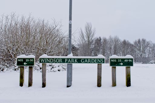 A wide angle shot of three signs giving directions in a park covered in snow