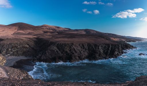 A panoramic shot of a sea inlet with crashing waves under a clear blue sky