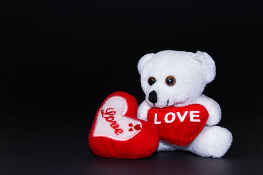 A plush teddy bear with a red heart in its hands on a dark background
