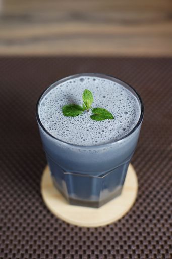 A vertical shot of a glass of blue shake with mint on top on the table with a blurry background