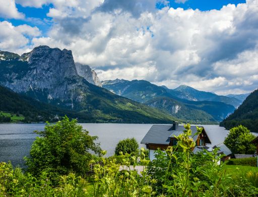 A beautiful shot of a landscape with  lake, mountains, houses, and cloudy sky