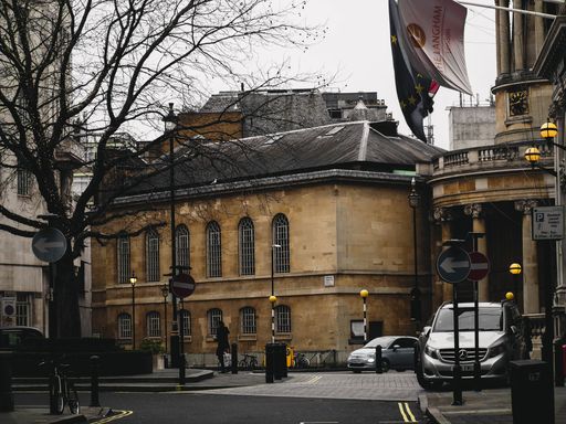 A person walking in front of a building in central London, cars and road signs around