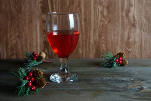 A closeup of a glass of red wine on the table with decorative holly berries on it