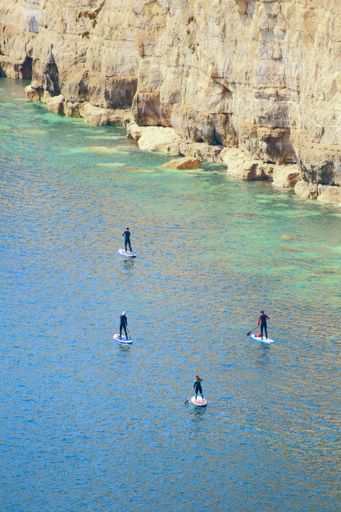 A vertical shot of surfers on the blue ocean near the rock