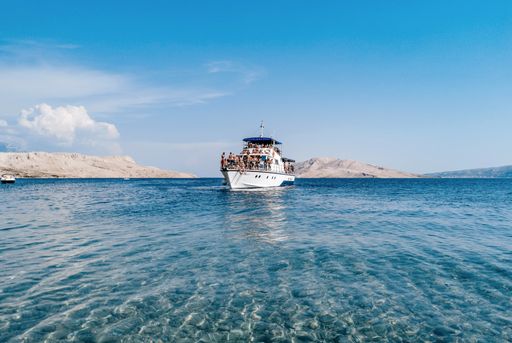 Small tourist ship full of people sunbathing on deck and enjoying excursion during summer holidays.