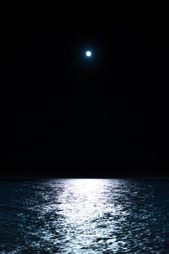 A vertical shot of a blue sea with the Moon on the background at night