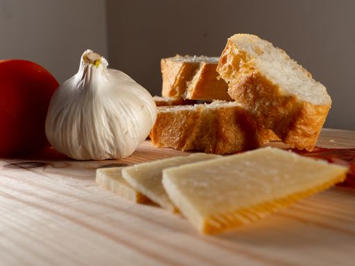 A closeup shot of the tomato, onion, sliced bread, cheese and sausage on a wooden cutting board