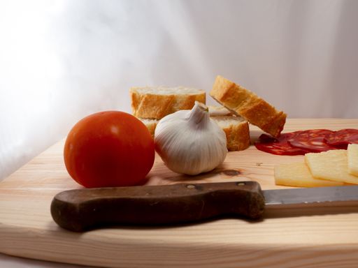 A closeup shot of the tomato, onion, sliced bread, cheese and sausage on a wooden cutting board