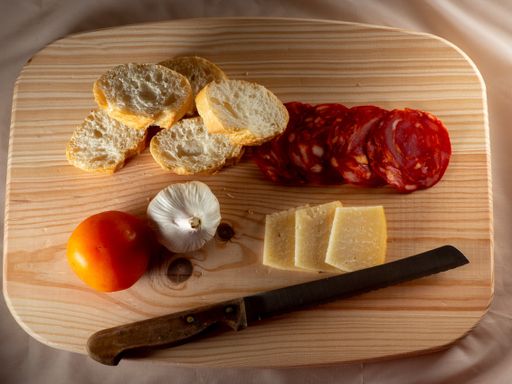 A top view of the tomato, onion, sliced bread, cheese and sausage on a wooden cutting board