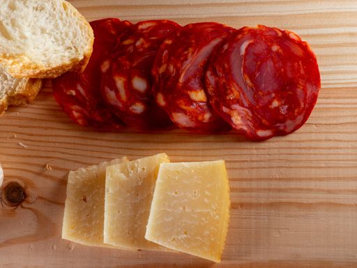 A top view of sliced bread, cheese and sausage on a wooden cutting board