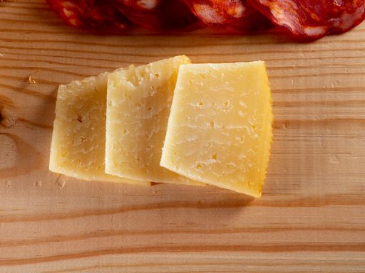 A top view of sliced cheese and sausage on a wooden cutting board