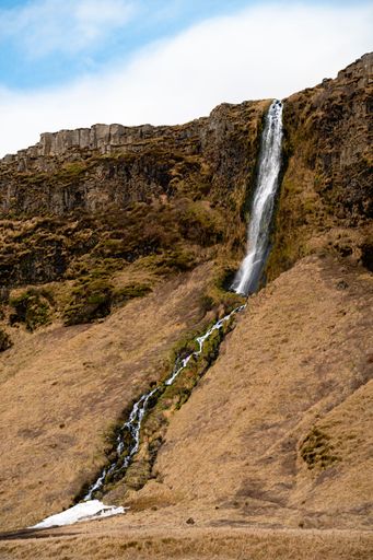 A stunning vertical shot of a waterfall cascading down rocky mountains in Iceland