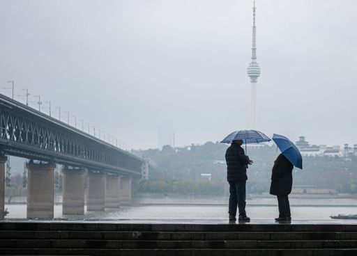 The two people standing side by side with umbrellas during rain