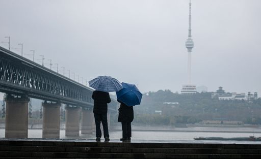 The two people standing side by side with umbrellas during rain