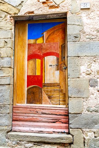 An old entrance door painted with graphic patterns in an old stone wall. The door is painted in the upper part and has crossbars in the lower part.