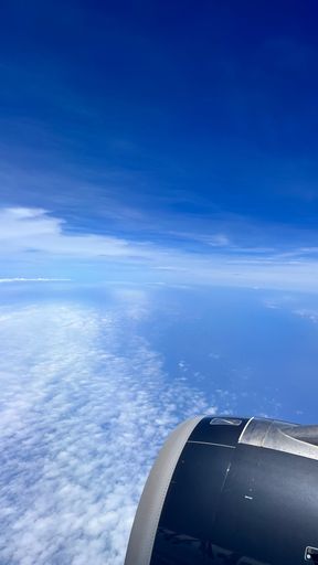 An aerial view of a jet engine soaring through the sky on a sunny day, with white and fluffy clouds dotting the deep blue sky