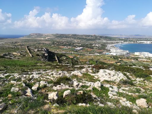 A scenic landscape featuring a rolling grassy hill on the shoreline, overlooking a tranquil ocean with calm blue waters
